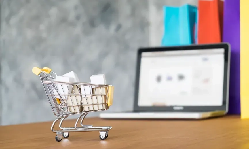 Miniature shopping trolley filled with parcels in front of a laptop and shopping bags