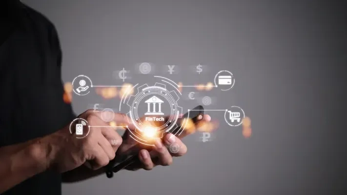 Hands using a phone surrounded by fintech icons for banking, cards and world currencies