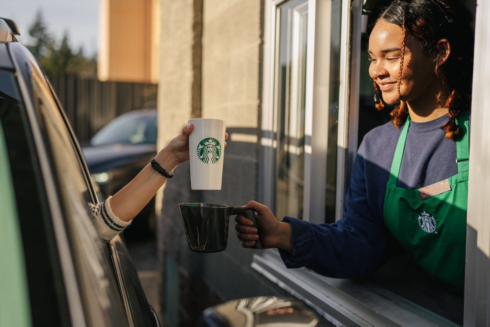 Starbucks drive-thru customer hands a reusable Starbucks cup to a barista, part of the reusable cup rewards program
