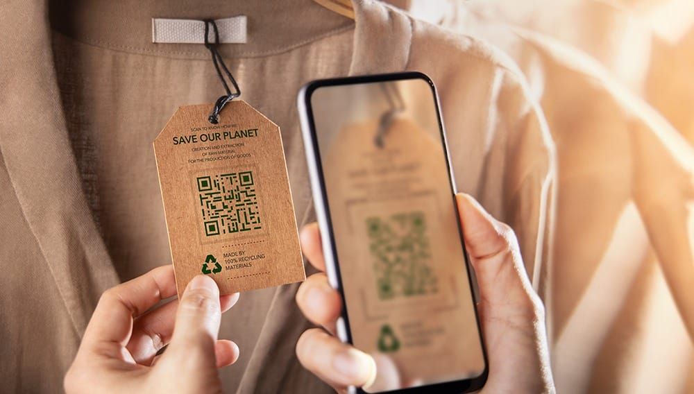 Shopper scans a Save Our Planet QR code tag on a garment with a smartphone, showing tech-driven green loyalty
